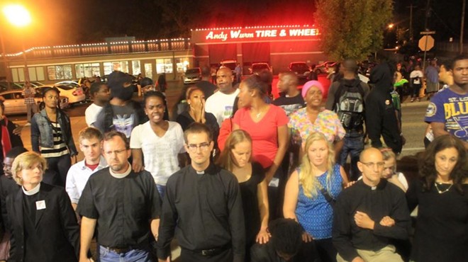 Several clergy members kneel down in prayer in front of the Ferguson Police Department.