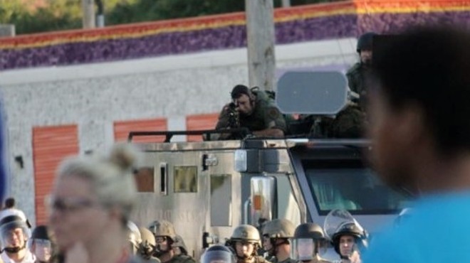 An officer on the scene in Ferguson peers down the scope of his rifle at an unarmed, peaceful crowd.