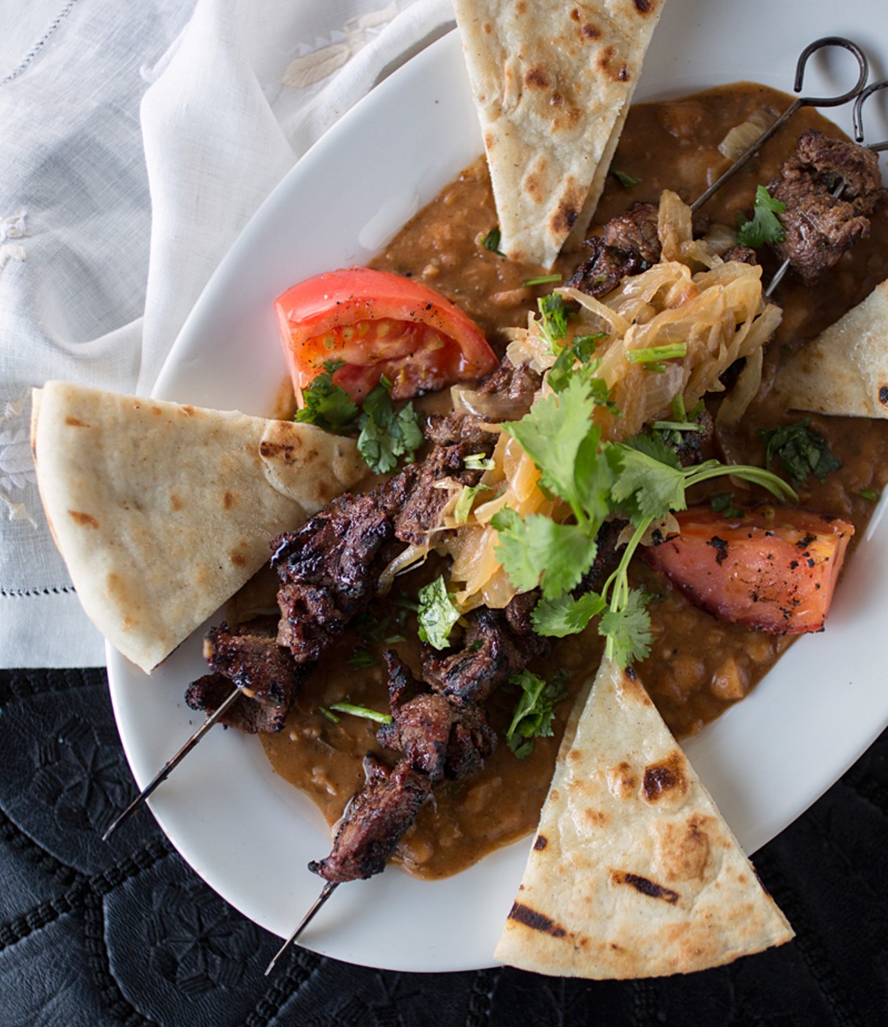 "Beef brochettes" is a grilled beef skewer with harissa, red charmoula sauce and flat bread, served with loubia.