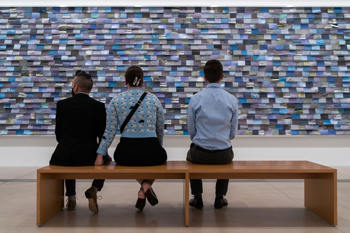 Three visitors sitting in front of Faye HeavyShield's work "aiyo niitahtaan," at the Pulitzer.