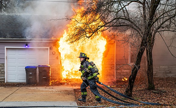 A firefighter with the Florissant Valley Fire Protection District stretches a water hose to extinguish a house fire on Friday, Jan. 26, 2024, in Florissant.