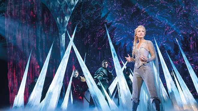 An actress dressed as Elsa from Frozen stands on a stage with ice spikes behind her.
