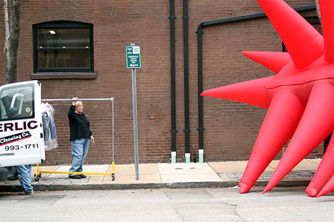 A woman holds onto a clothes rack, gazing at the giant red blob.