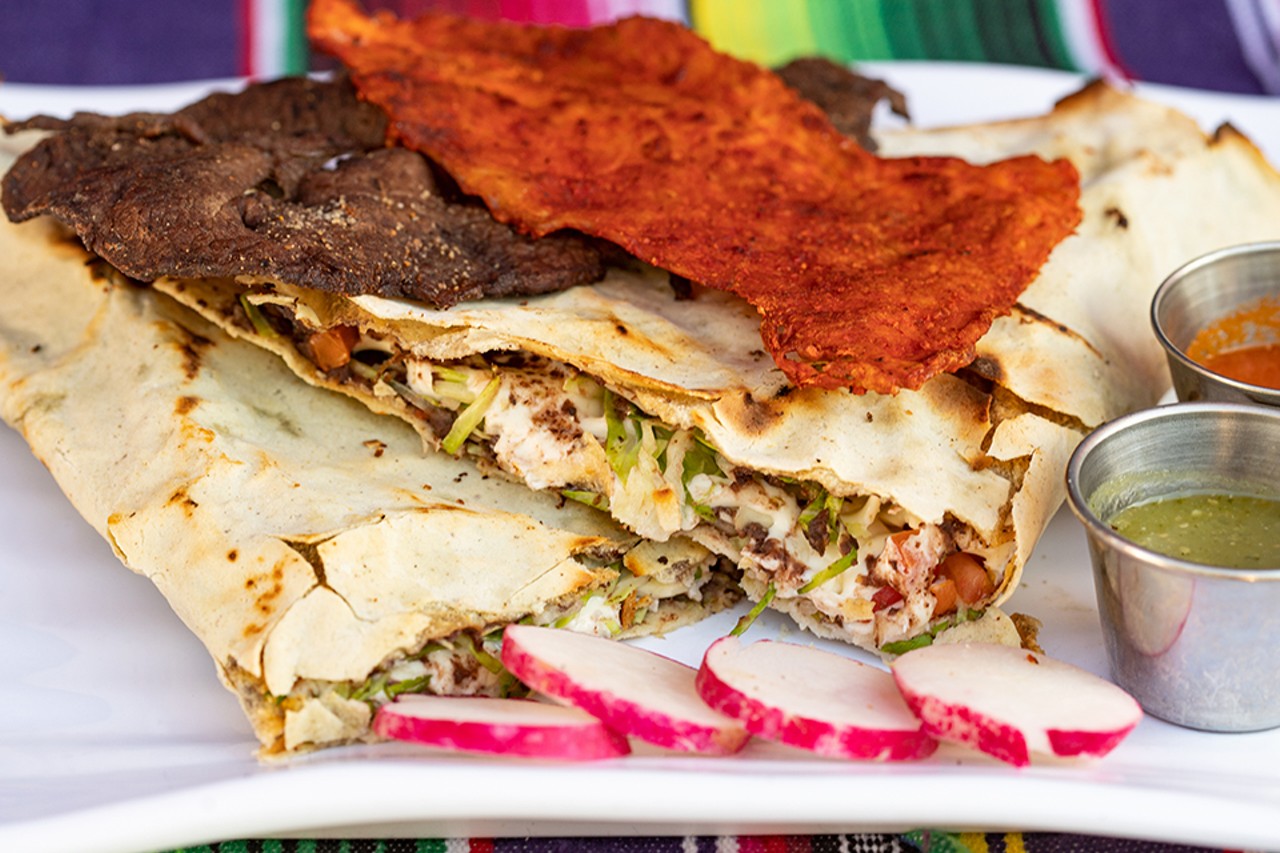 Tlayuda, a hardened tortilla filled with refried black beans, asiento (unrefined pork lard), cabbage, meat, avocado and Oaxaca cheese.