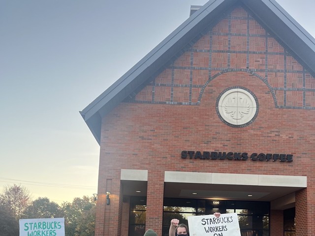 People hold up signs in front of a brick building that reads "Starbucks Coffee."