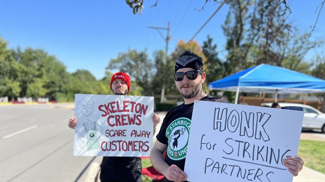 Two people hold signs on the edge of a road that read "skeleton crews scare away customers" and "honk for striking partners."