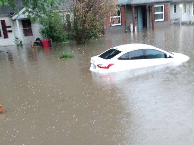 A white car underneath water that has flooded an entire street.