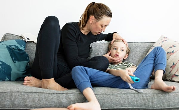 A woman holds her son's head as they sit on a couch.