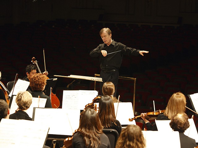 A conductor stands in front of a group of violinists.