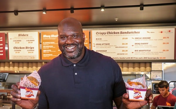 Shaquille O'Neal stands in front of Big Chicken holding two orders.