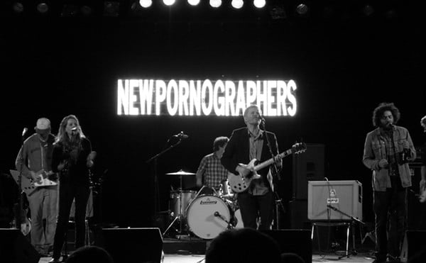 A band plays in front of a sigh that reads "New Pornographers."