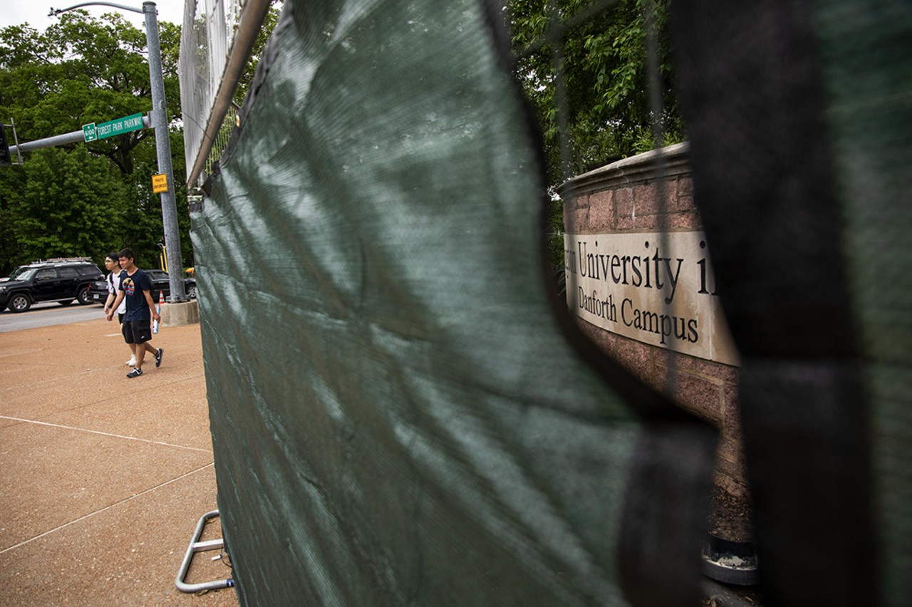 Students walk past a metal fence covered by a green tarp on Wash U’s Danforth Campus.