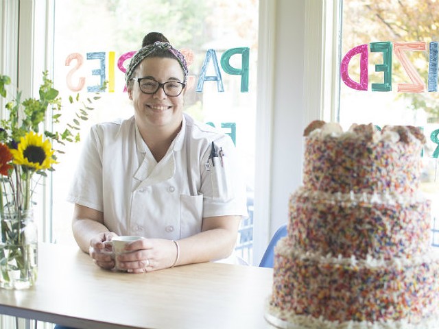 Alex McDonnell sits at a table next to a three-tier cake in Prioritized Pastries.