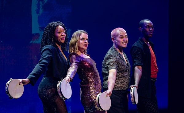 Four people hold tambourines on stage.
