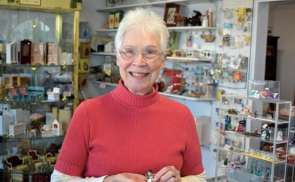 Meg Dietrich smiles in a red sweater as she holds a mini snowman in front of a range of collectible objects.