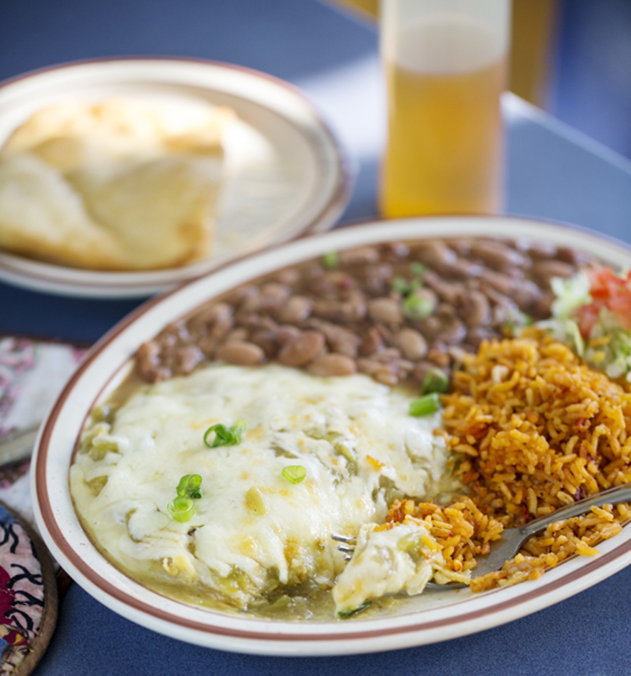 Green Chile Enchiladas - stacked corn tortillas with Monterrey jack and green chile. You can add chicken, beef, chorizo, veggie chorizo or calabacitas. Top with a fried egg. Comes served with pinto beans and rice.