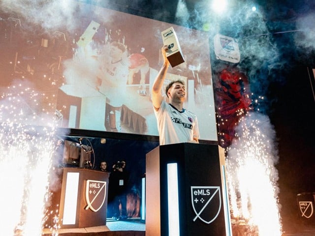 Niklas Raseck holds the eMLS trophy on stage as sparks and smoke surround him.
