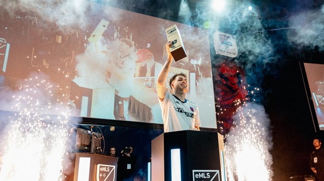 Niklas Raseck holds the eMLS trophy on stage as sparks and smoke surround him.