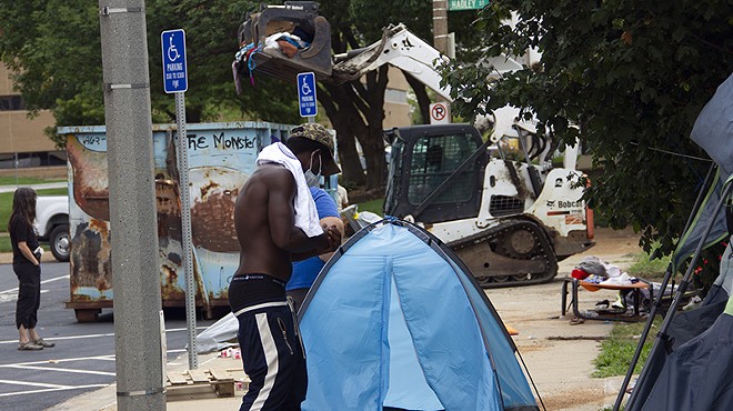 An unhoused resident of Interco Plaza gathers the contents of his tent as city workers clear the encampment.