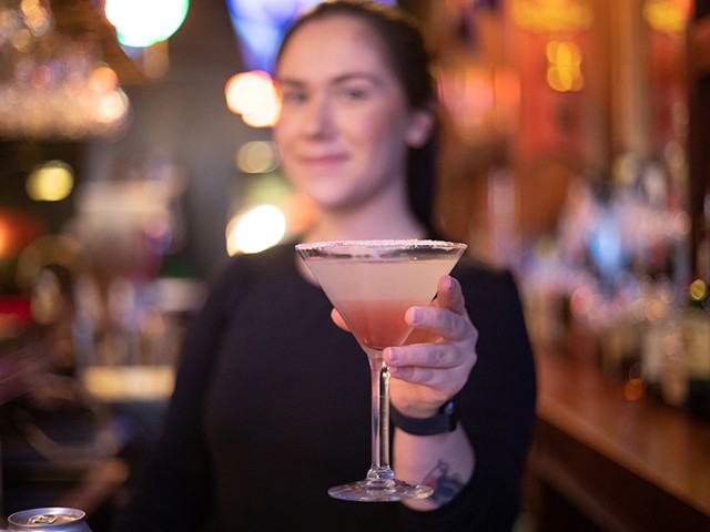 A bartender holds out a martini to the viewer.