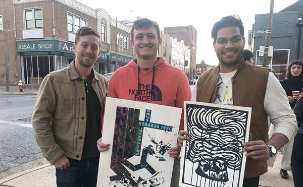 Three men stand together and two hold up prints from the Print Bazaar.