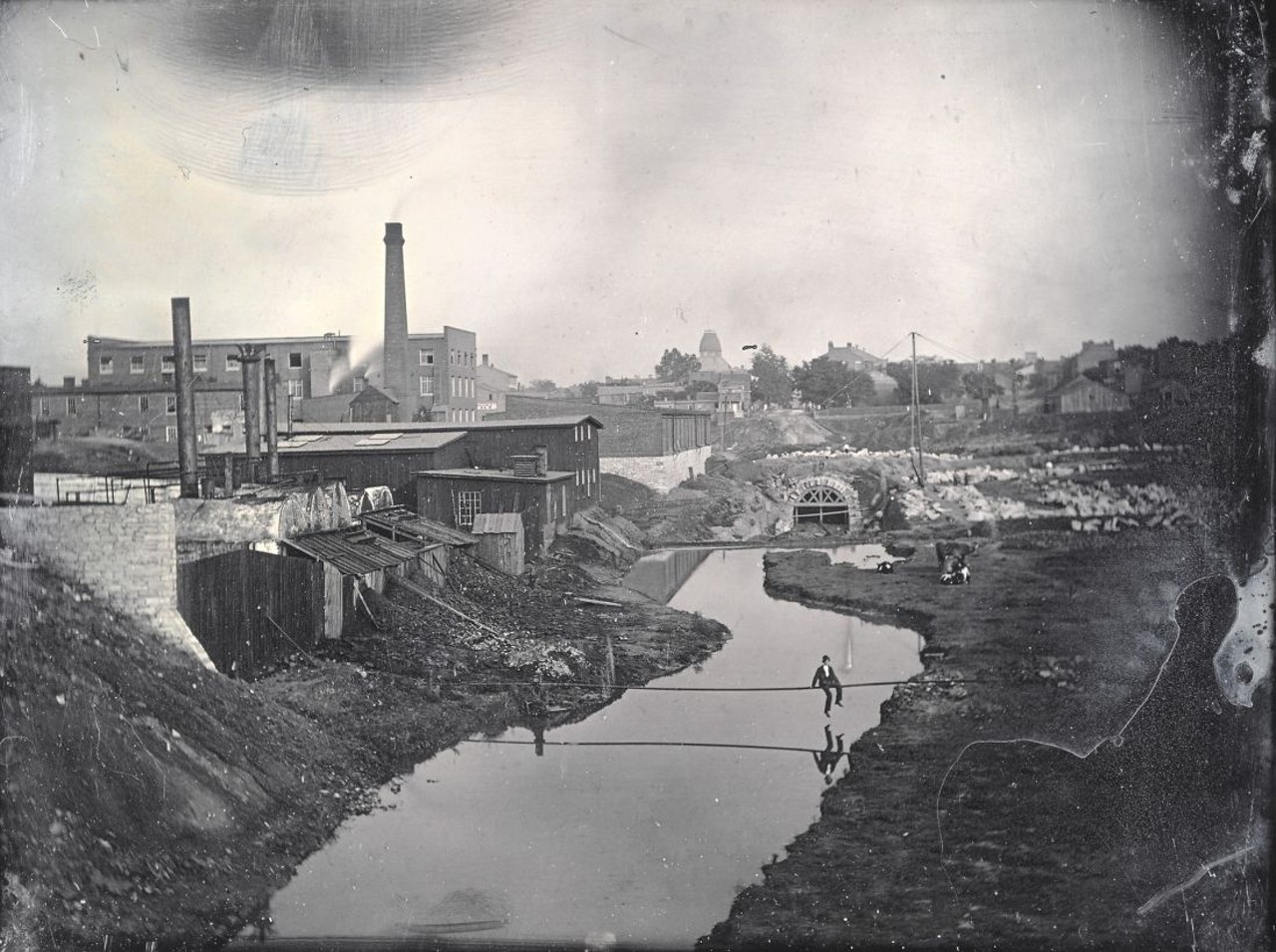 MILL CREEK SEWER UNDER CONSTRUCTION NEAR TENTH STREET, 1868
"The Mill Creek sewer had a 20-feet-wide opening and required structural walls nearly 6 feet thick. St. Louis's natural bedrock formed its bas, and where there was no stable bedrock to be found, 9-inch square timbers were used." &#151; Andrew Wanko, 'Great River City'
Chouteau's Mill Creek, East from Thirteenth and Gratiot showing construction of the Mill Creek Sewer. A man can be seen sitting on the pipe over the stream. Daguerreotype by Thomas M. Easterly, 1868. Missouri Historical Society Collections.