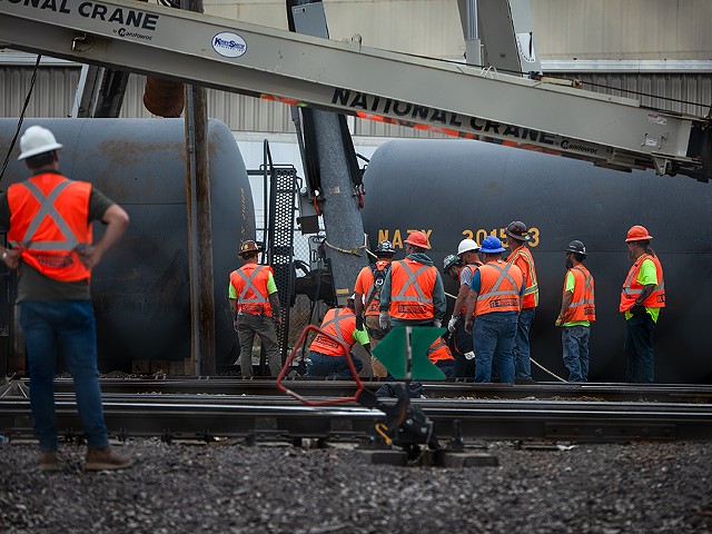 Crews work to attach cables to derailed railcars.