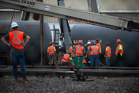 Crews work to attach cables to derailed railcars.