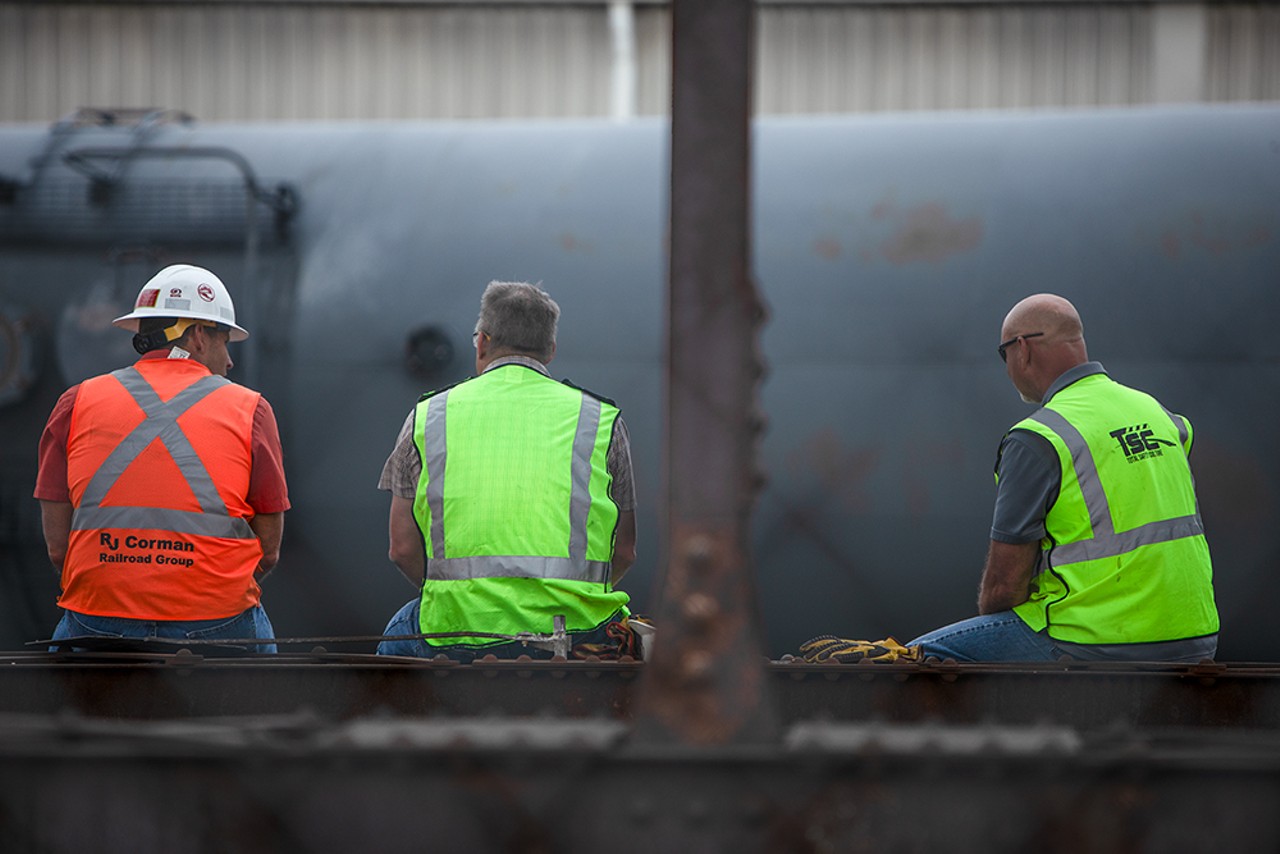 Three workers take a break from flipping derailed tankers upright.
