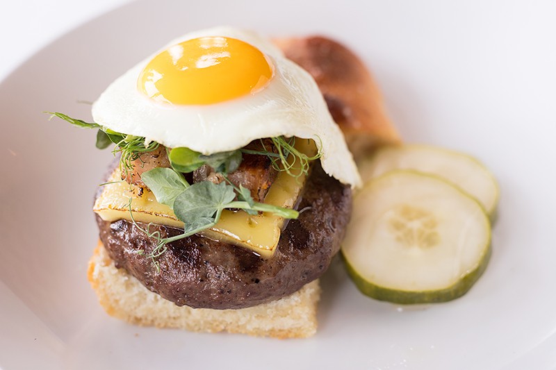The burger is topped with a fried chicken egg and served on sea-salt foccacia with house pickles. - MABEL SUEN