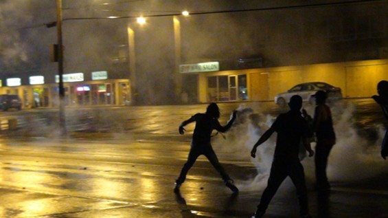 A protester throws a tear-gas canister back at the police who shot it. - Ray Downs