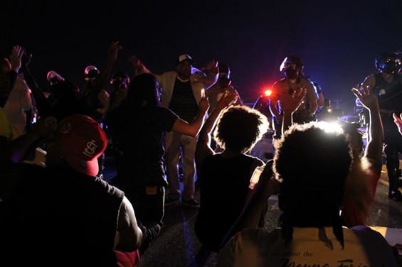 Protesters kneel down and put their hands up in front of police. - Ray Downs