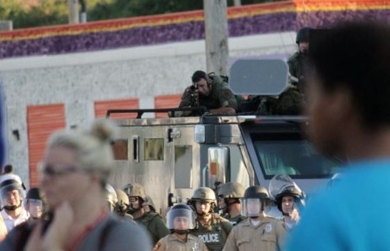 An officer in Ferguson peers down the scope of his rifle at an unarmed, peaceful crowd. - Danny Wicentowski