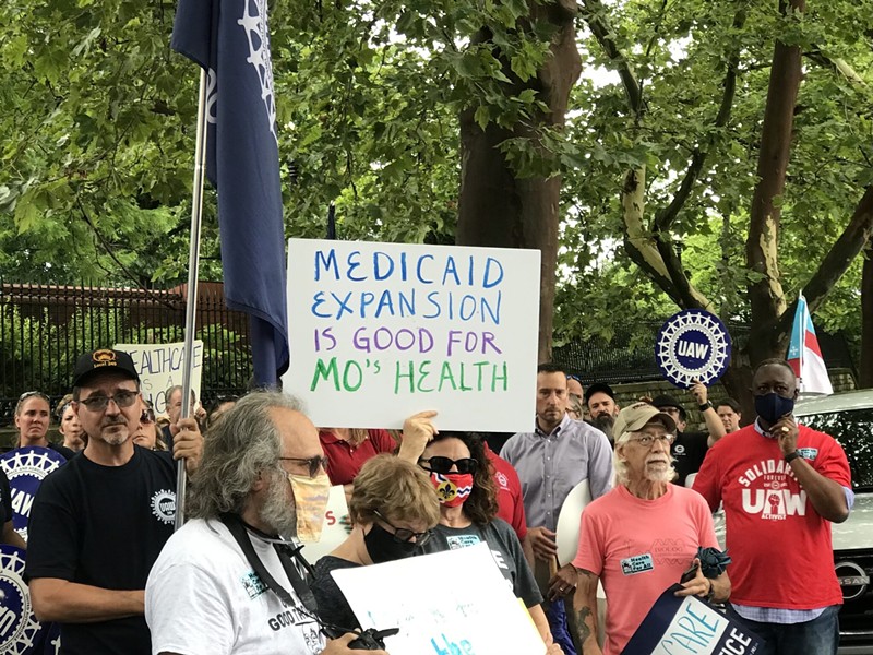 Demonstrators stand outside of the Governor's Mansion in Jefferson City on July 1, 2021 and hold signs urging Gov. Mike Parson to fund voter-approved Medicaid expansion. - Tessa Weinberg / Missouri Independent