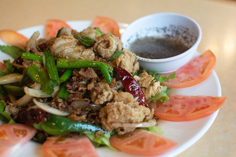 Muc Xao Gion: crispy calamari stir fried with green peppers, scallions and red chili peppers. Served with a special pepper lemon sauce on a bed of lettuce, tomatoes and onions - ANDY PAULISSEN