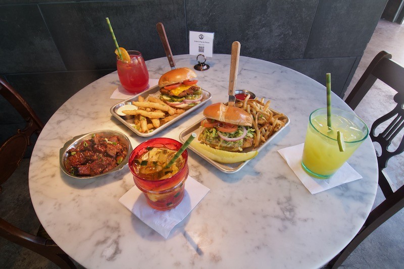 A selection of Station No. 3's offerings (from far right, clockwise) Diego’s Margarita, the Station burger with pickle fries and ranch, Pimm’s Cup, burnt ends, Frida’s Hibiscus Margarita and  barramundi Sandwich with skinny fries. - Lulu Nix
