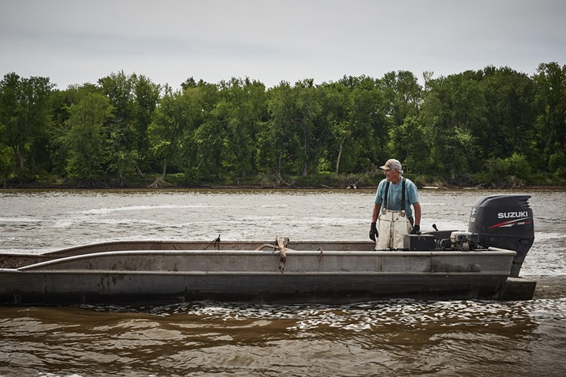 A fisherman stands in a motor boat on a river.