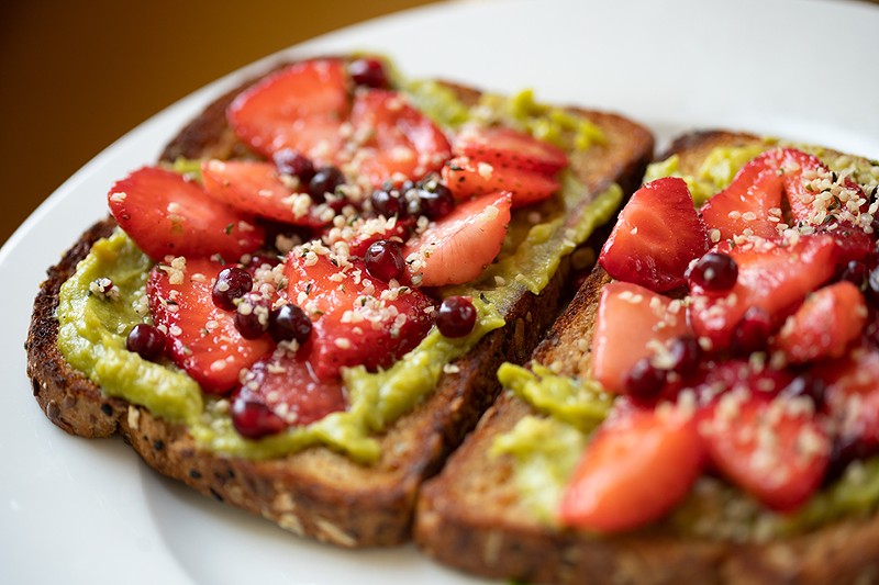 Avocado toast features whole grain bread, smashed avocados, strawberries, pomegranate arils, hemp seeds and sea salt.