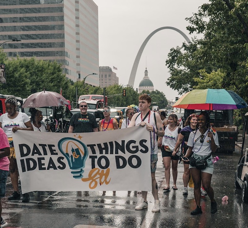 People walk in front of the Arch holding a sign that reads "Date Ideas & Things To Do STL."