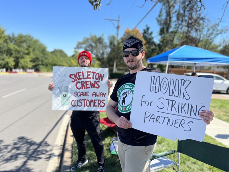 Two people hold signs on the edge of a road that read "skeleton crews scare away customers" and "honk for striking partners."