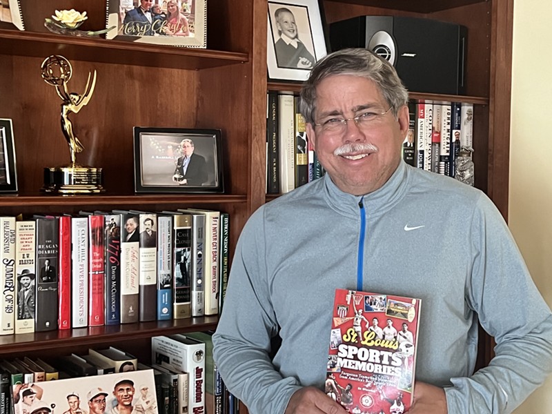 Ed Wheatley holds his book St. Louis Sports Memories in front of a book shelf.