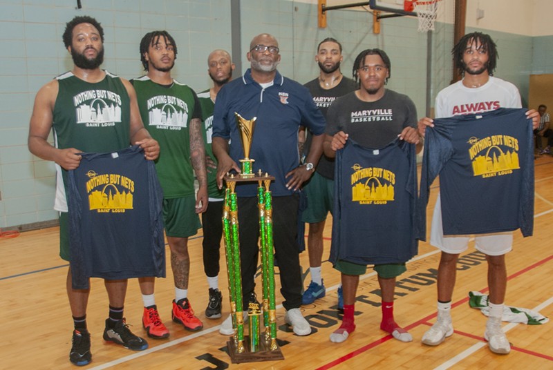 Six players and one coach pose. They hold championship t-shirts. A multi-foot-tall trophy sits in front of them.