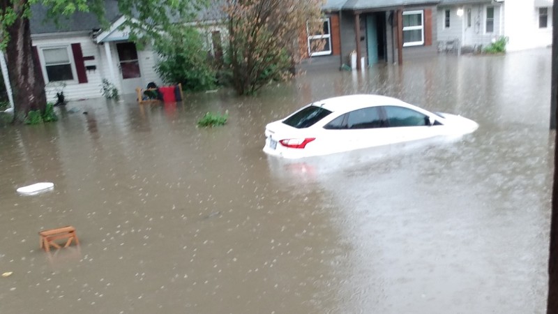 A white car underneath water that has flooded an entire street.