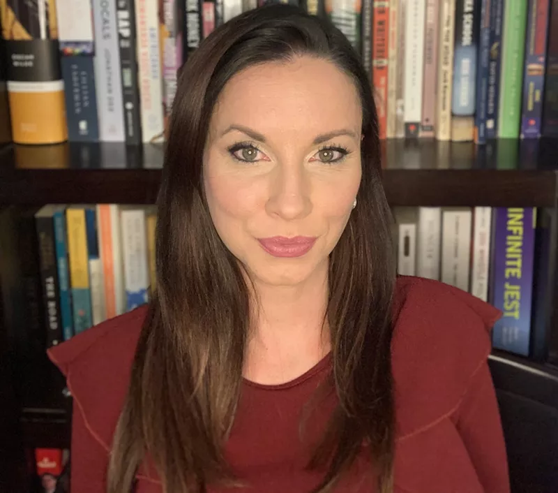 Anita Manion sits in front of a book shelf in a red shirt.