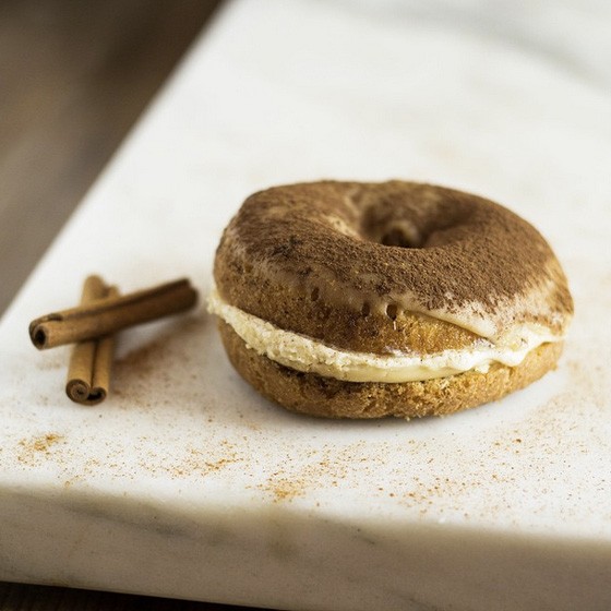 A tiramisu donut with cinnamon is photographed on a white table.