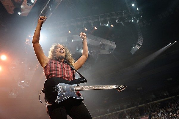 A Metallica band member holds his hands above his head with a guitar draped over his body.