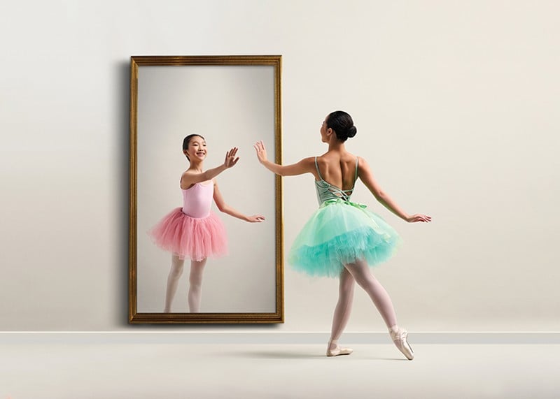A dancer reaches toward another dancer in a mirror.