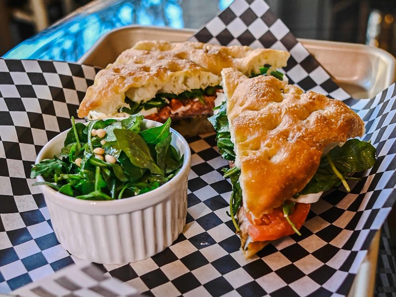 A caprese sandwich on focaccia, served with a side greens salad.