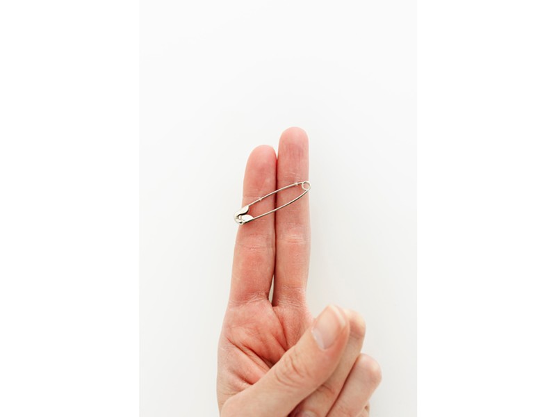 A pin pierces the skin of two fingers.