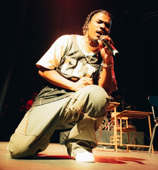 Smino kneels on stage while holding a microphone.